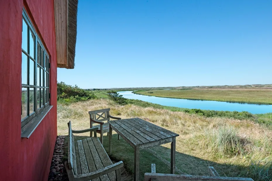 An outdoor seating area beside a red building overlooks a river and grassy landscape.