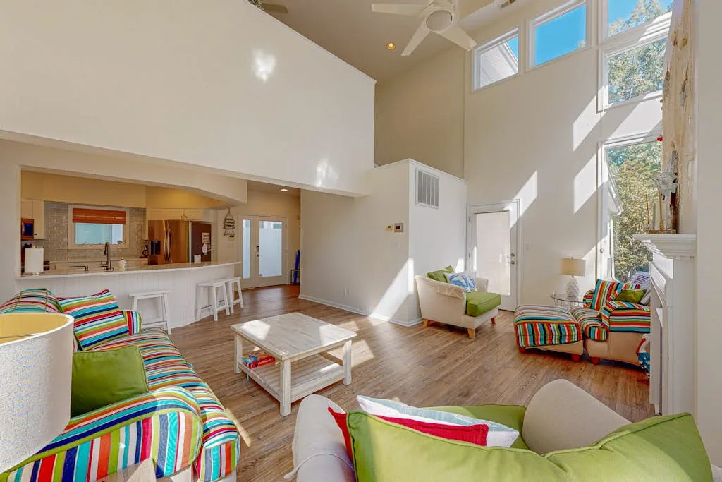 A bright living room with colorful seating, a coffee table, and tall windows.