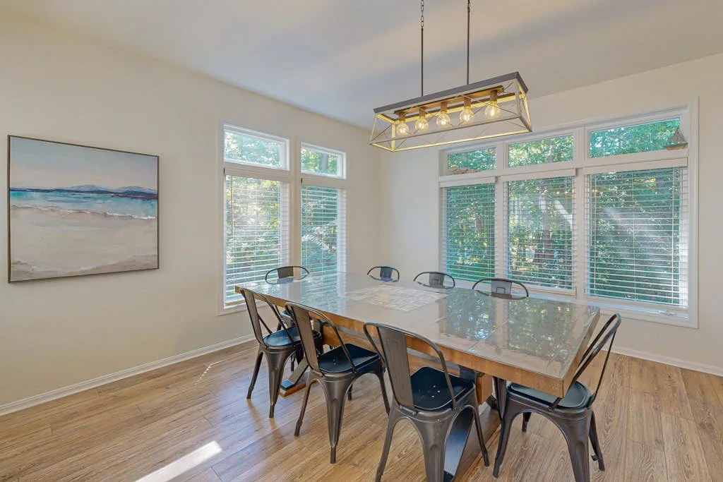 A dining area with a long table and windows overlooking greenery.