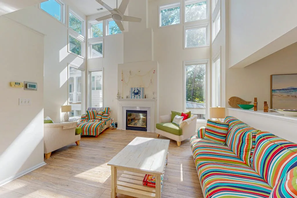 A bright living room with tall windows, a fireplace, and colorful striped seating.