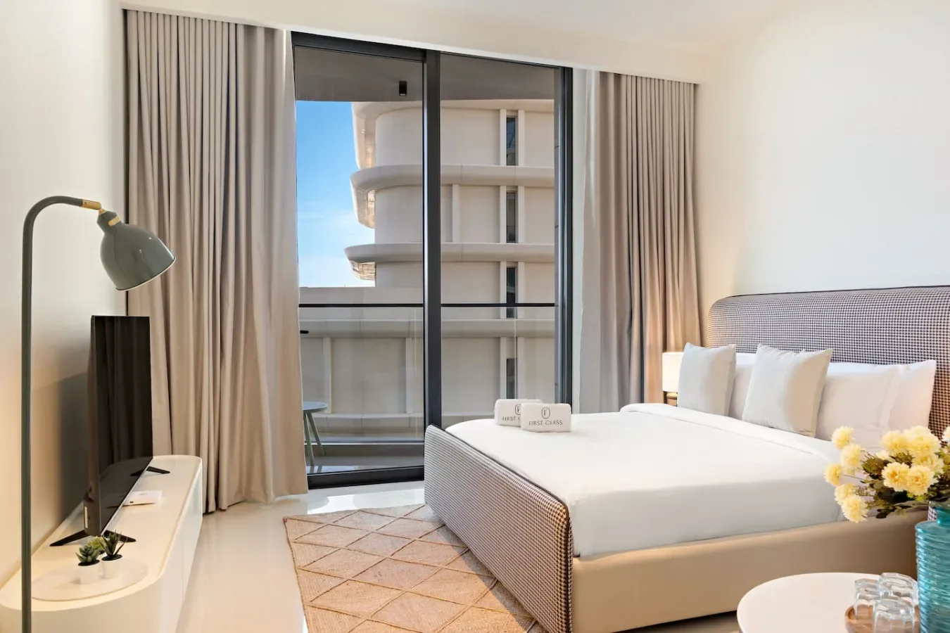 Un dormitorio luminoso con una cama junto a puertas de vidrio y cortinas largas.