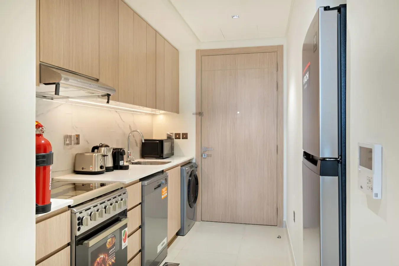 Una cocina compacta con armarios de madera clara, electrodomésticos y refrigerador.