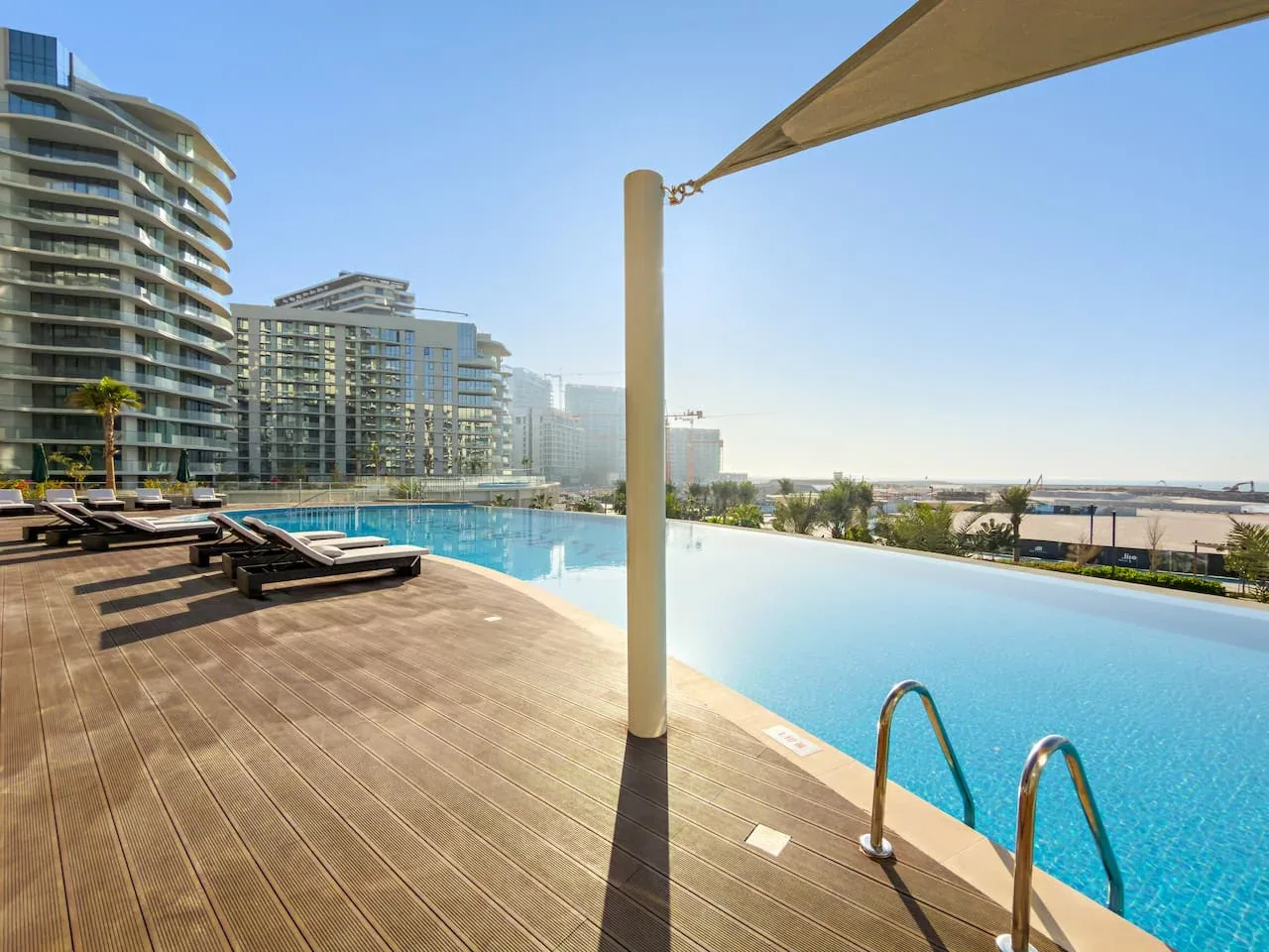 Una piscina al aire libre junto a una terraza de madera, con edificios altos al fondo.