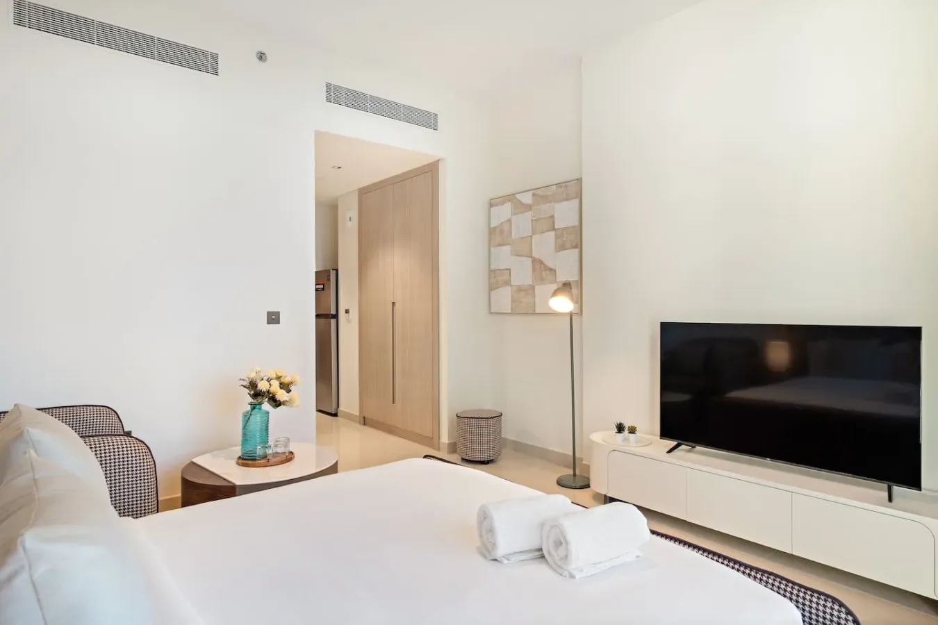 Un dormitorio luminoso con cama, televisor y lámpara de pie.