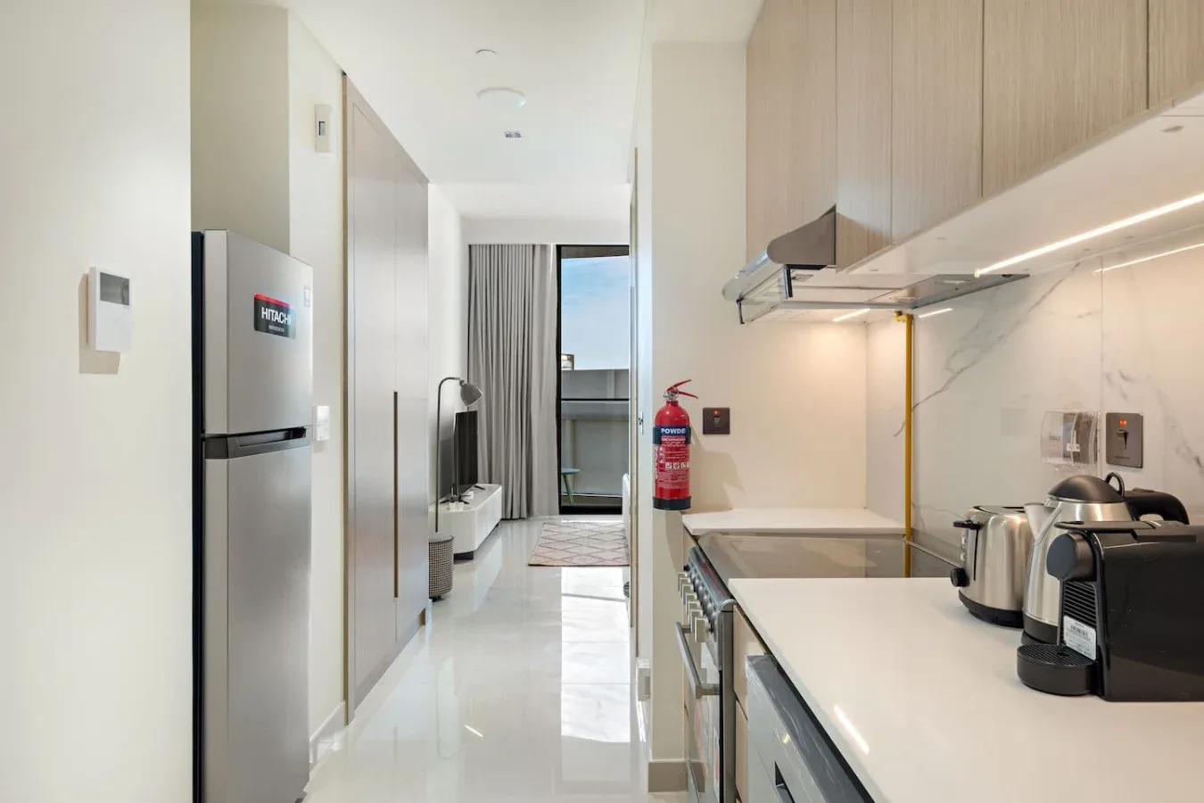 Una cocina moderna se abre a una sala de estar, con refrigerador y pequeños electrodomésticos sobre la encimera.