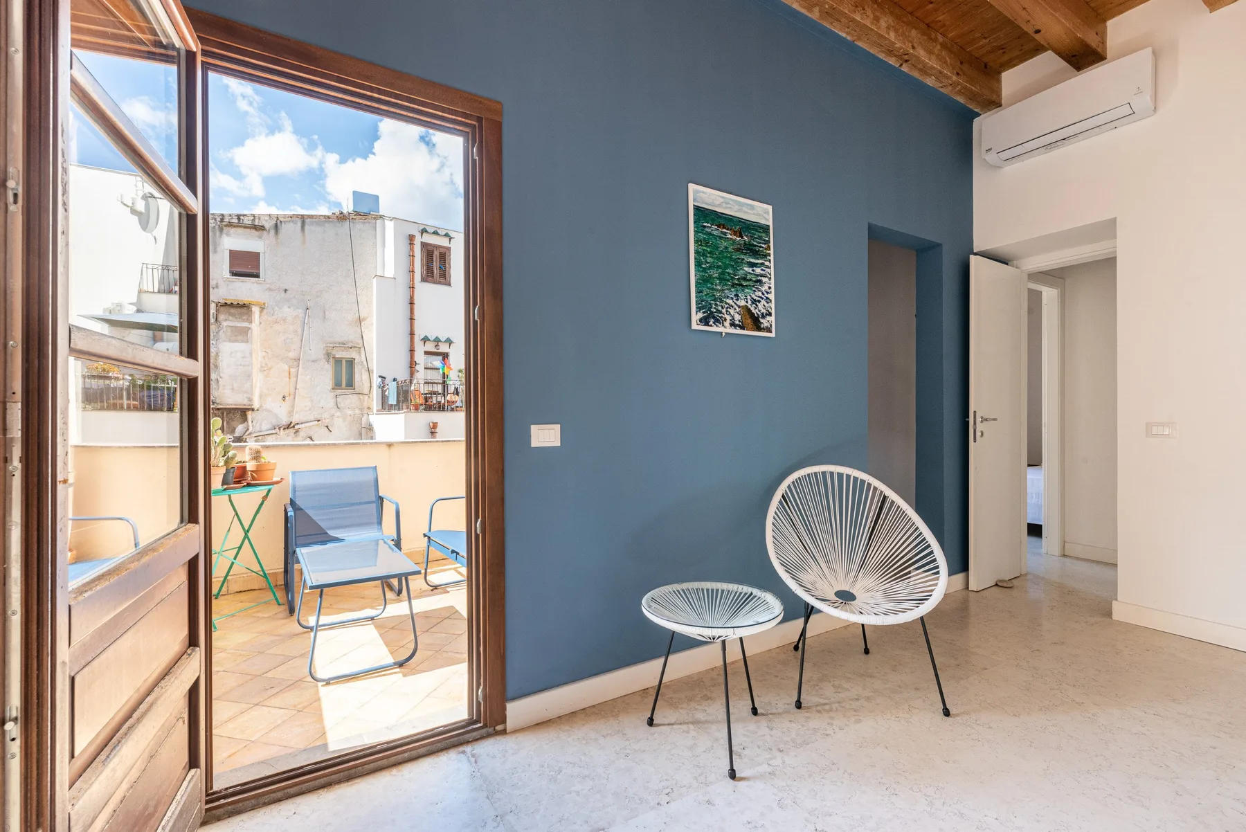 A bright living area with two woven chairs beside an open balcony door.