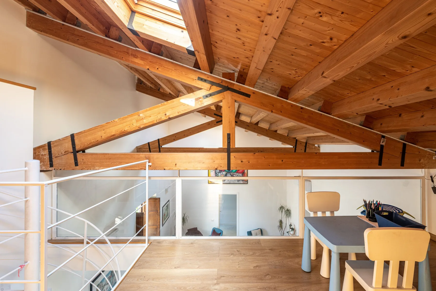 A loft workspace with a desk and chairs beneath exposed wooden beams.