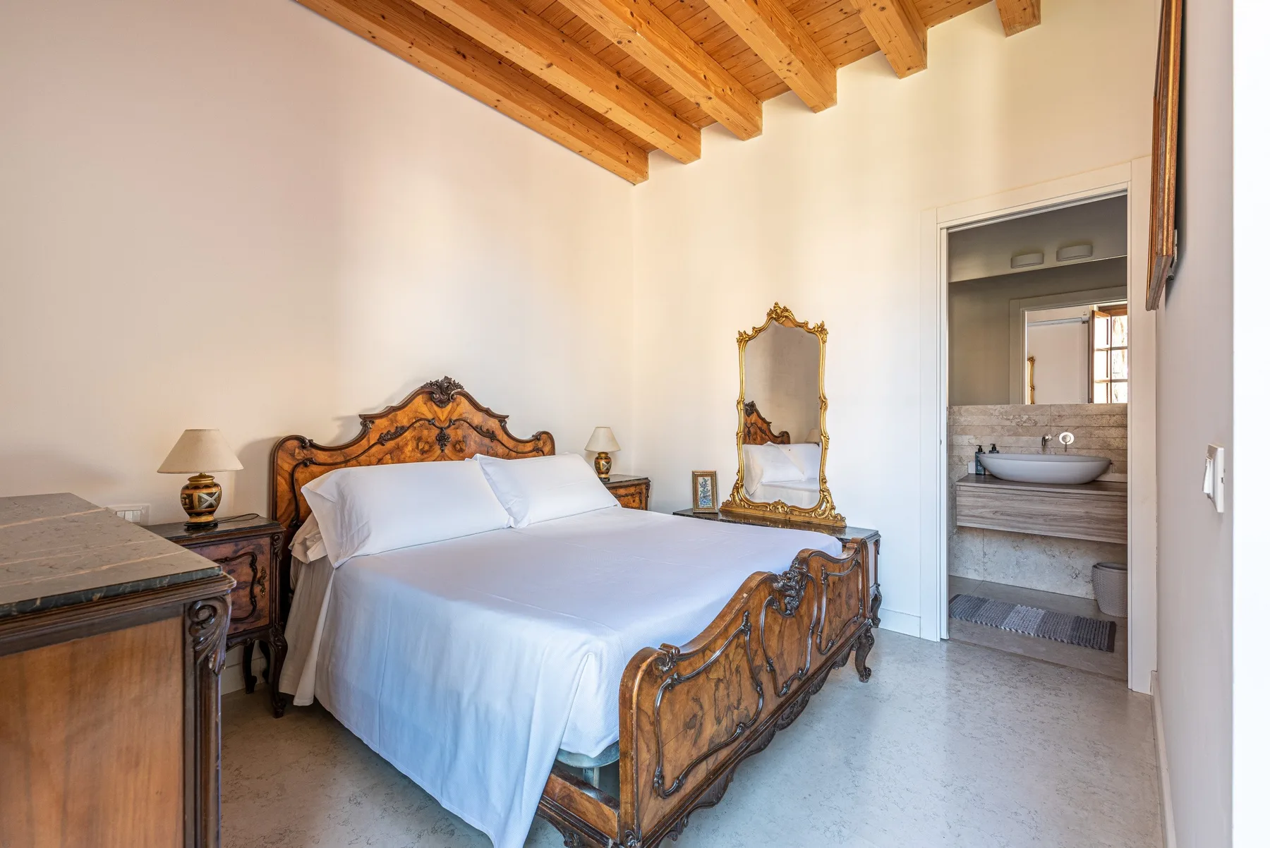 A bedroom with a carved wooden bed and an open doorway to a bathroom.