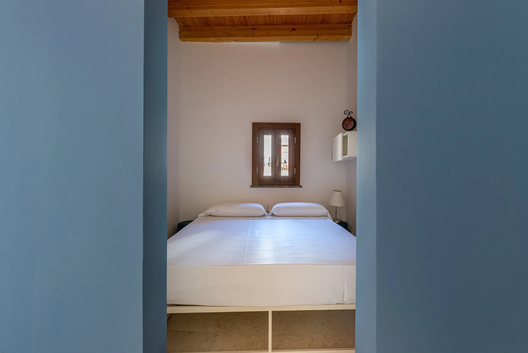 A bedroom with a neatly made bed beneath a small window.