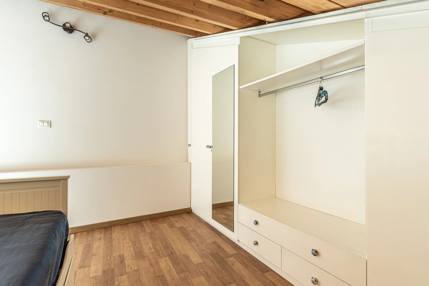 A bedroom with a bed beside an open wardrobe and wood flooring.