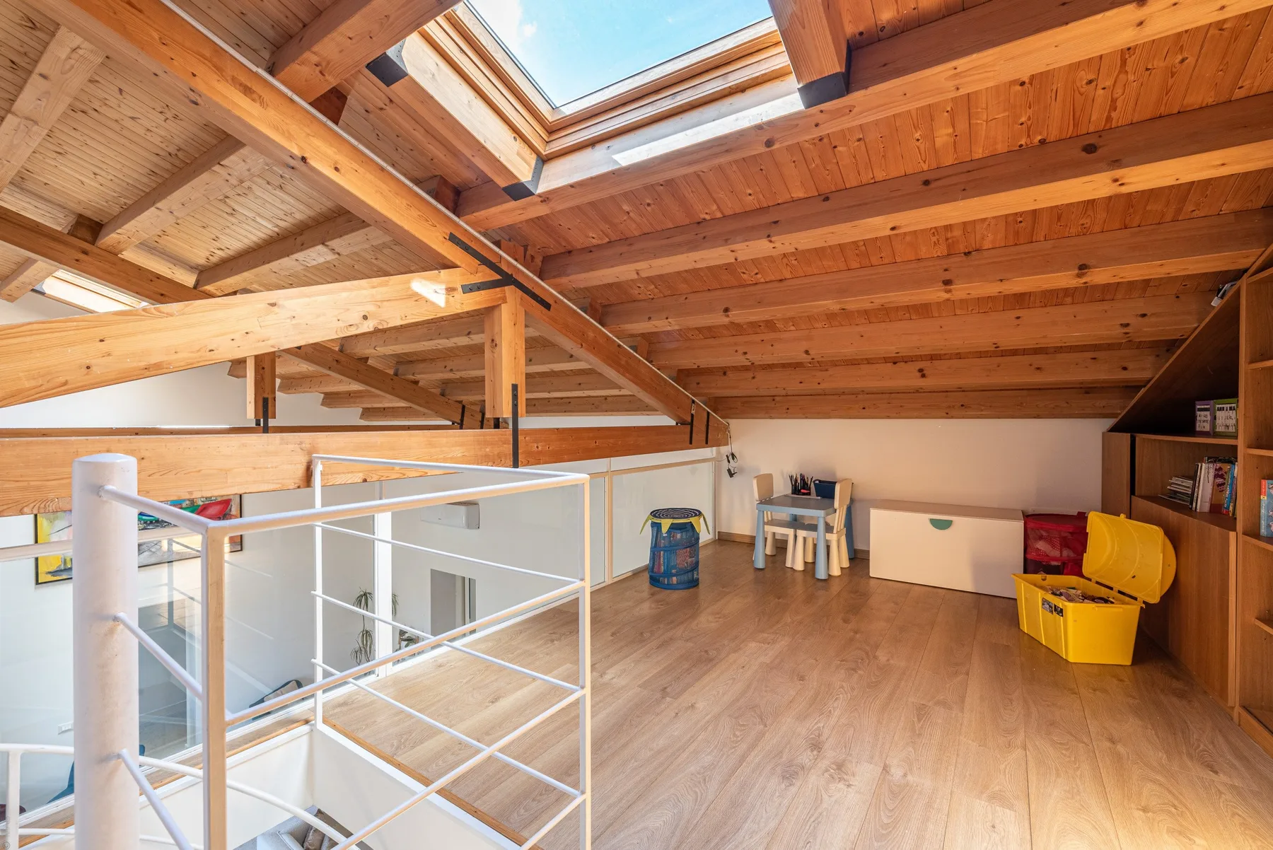 A wood-beamed loft space with a skylight and a small seating area.