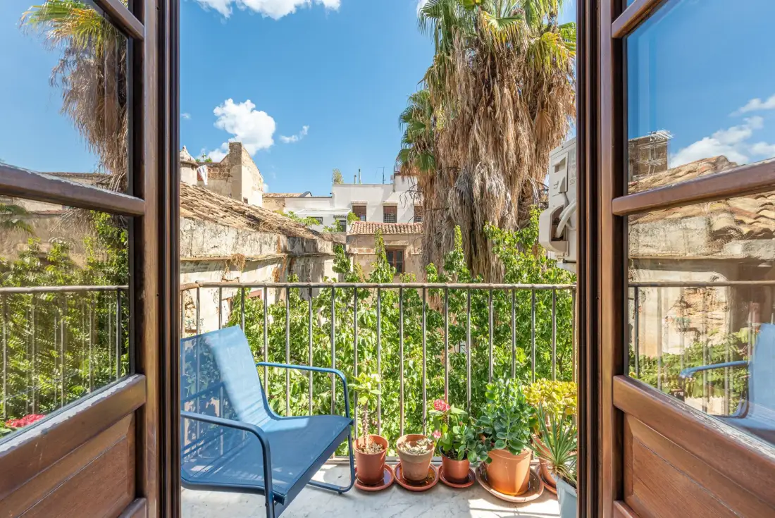 A balcony garden with a blue chair overlooks nearby buildings.