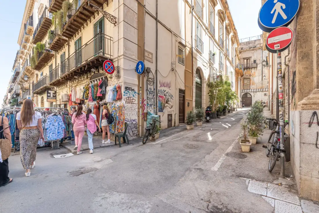 A narrow urban street lined with buildings, shops, and pedestrians.