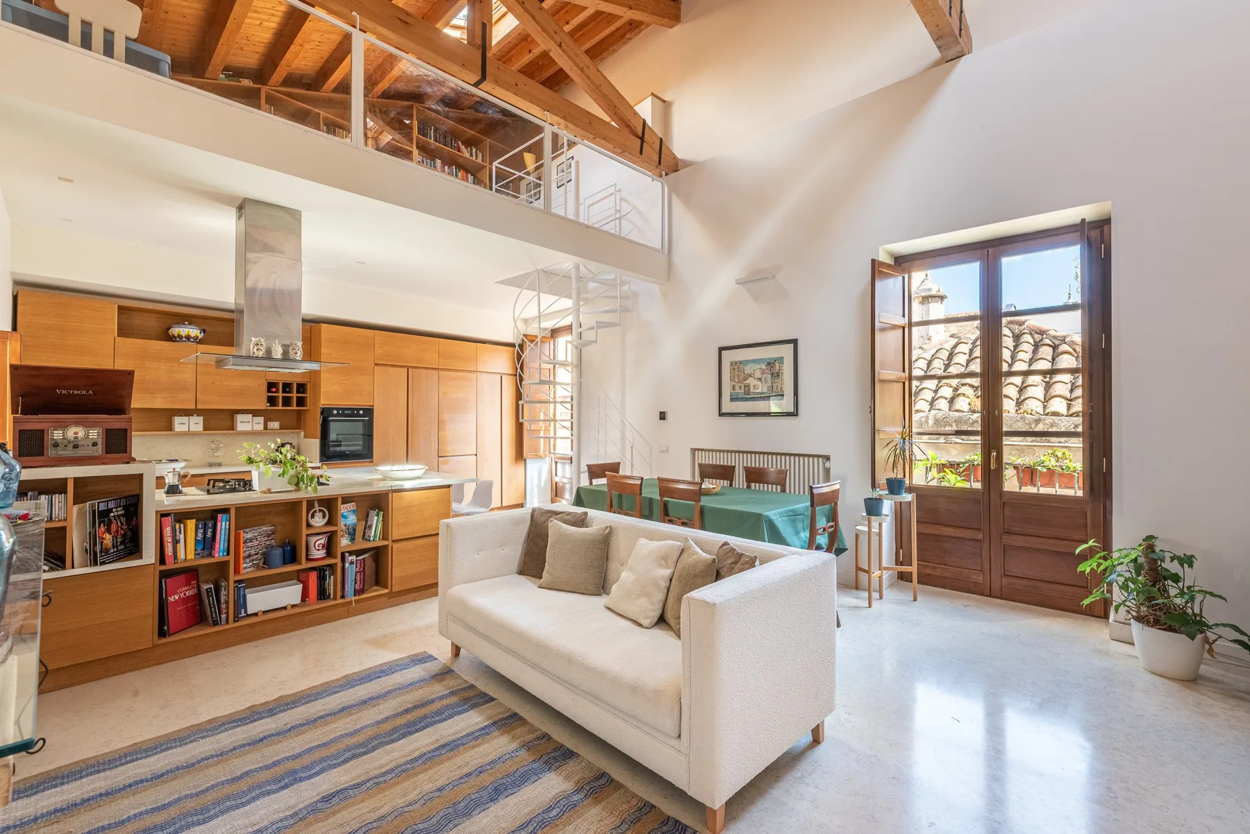 A bright open-plan living room and kitchen with a seating area beneath exposed wooden beams.