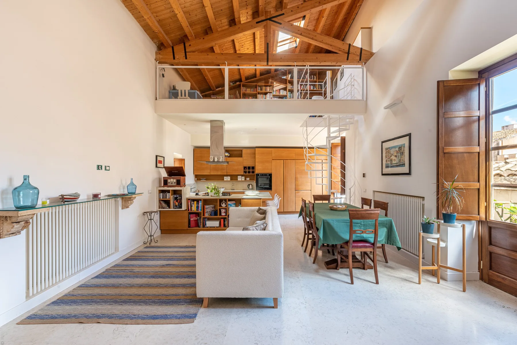 A bright open-plan living and dining room has a high exposed timber ceiling.