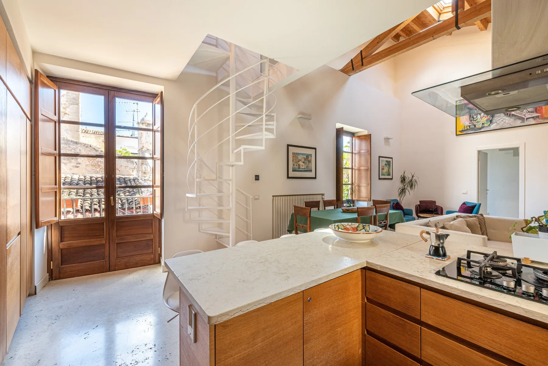 A bright open-plan kitchen and living area with a white spiral staircase.