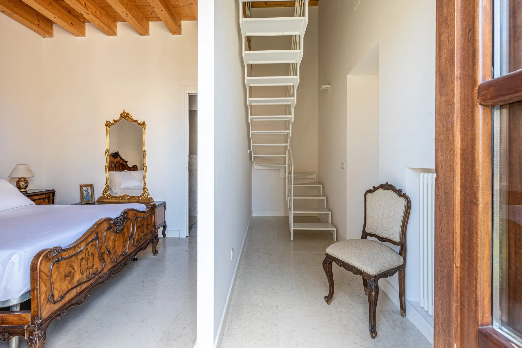 A bedroom with an ornate wooden bed and a narrow stairway beside it.