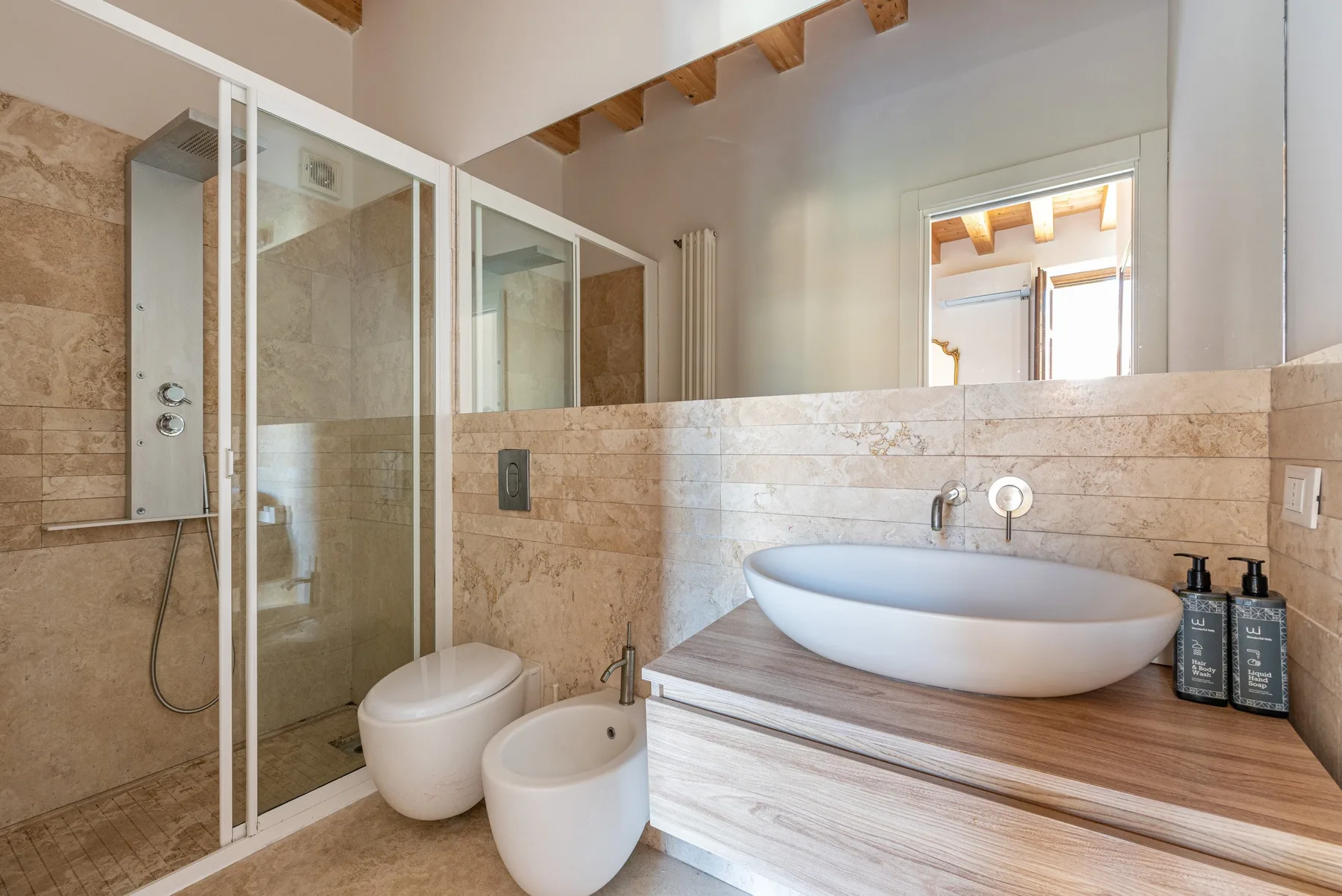 A bright bathroom with a glass shower, toilet, bidet, and vessel sink.