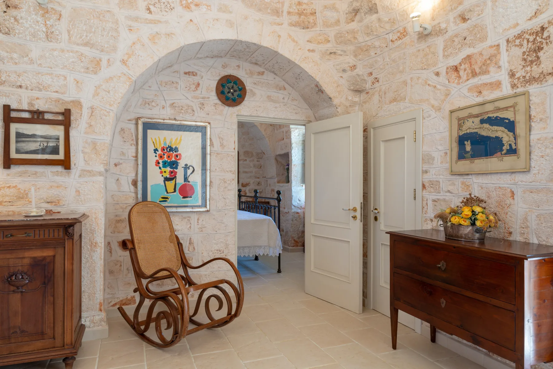 Una habitación de paredes de piedra con un arco, una mecedora y muebles de madera.