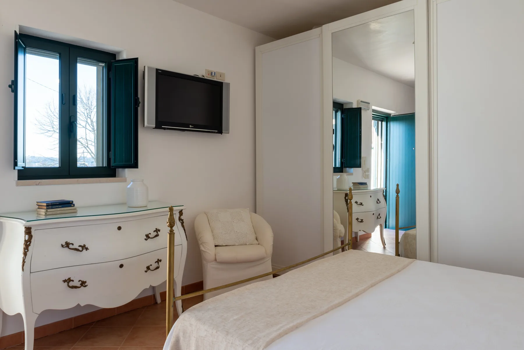 Un dormitorio con una cama, un armario con espejo y un televisor montado en la pared.