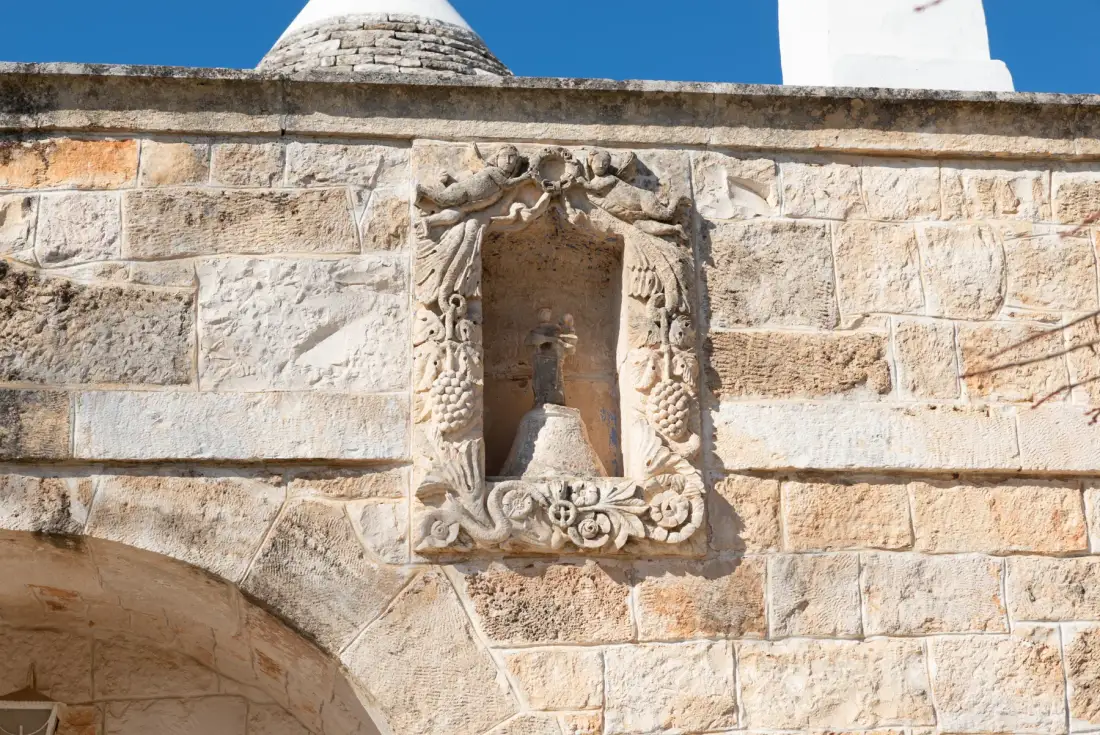 Un muro de piedra presenta un nicho tallado y ornamentado sobre un arco amplio.
