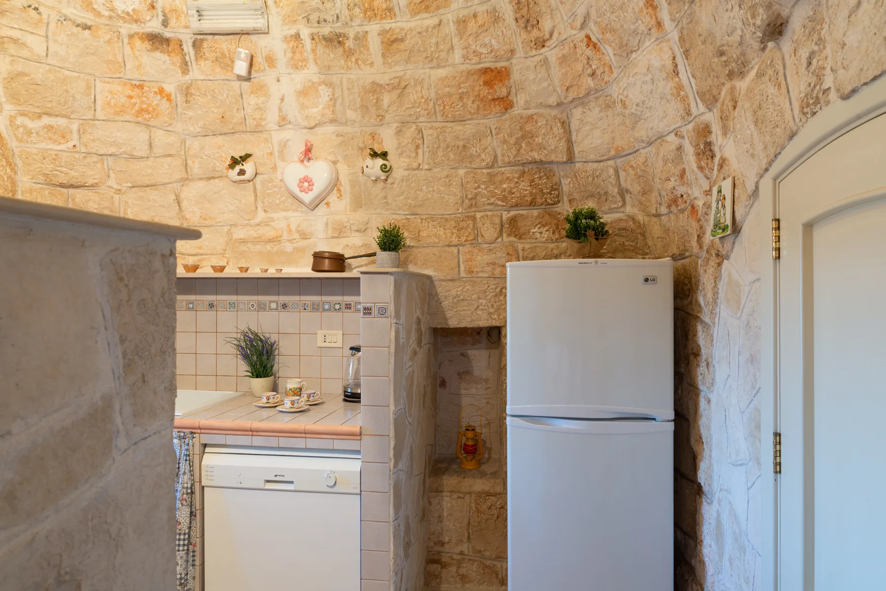 Una cocina pequeña con refrigerador, encimera de azulejos y paredes de piedra.