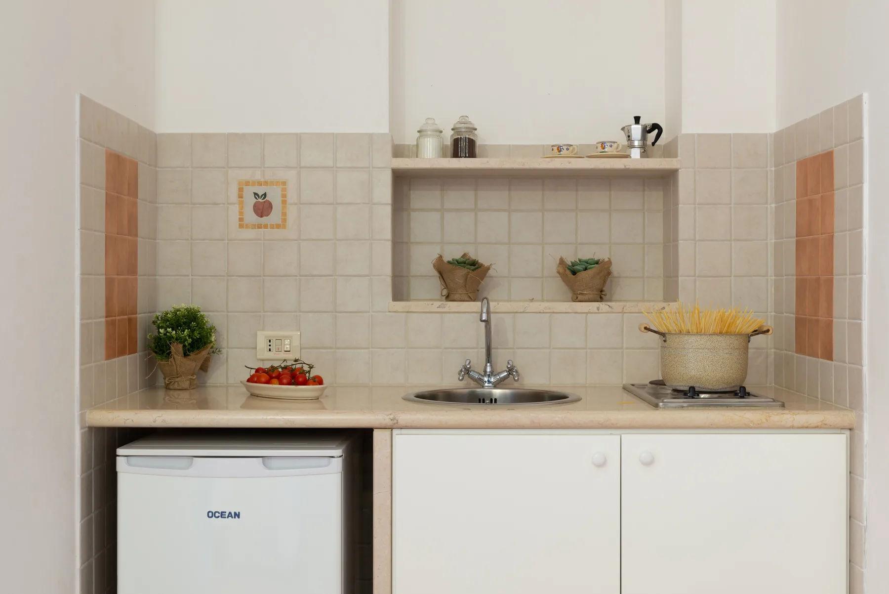 Una pequeña cocina con azulejos, fregadero, encimera y refrigerador compacto.