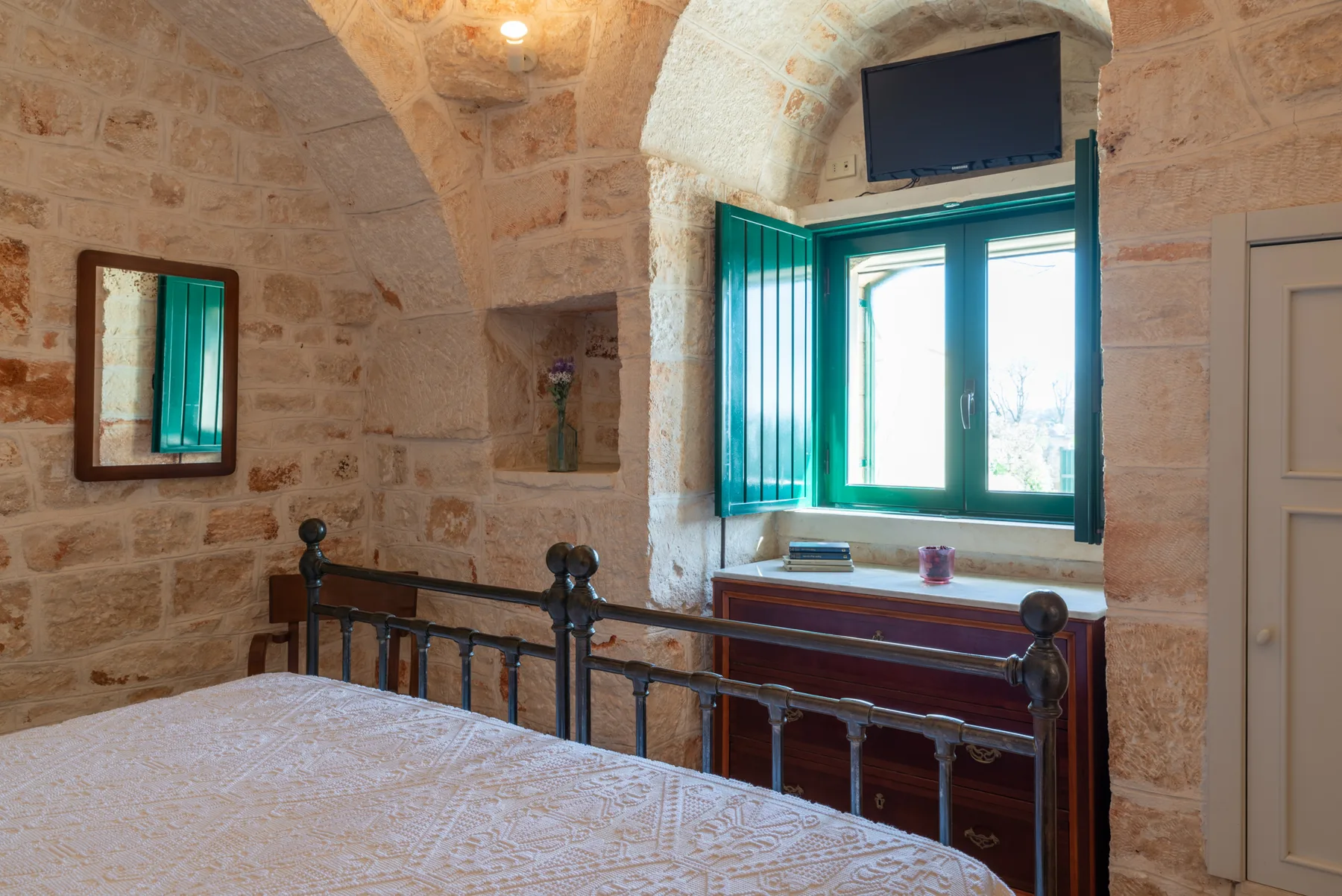 Un dormitorio con una cama, paredes de piedra y una ventana con contraventanas verdes.