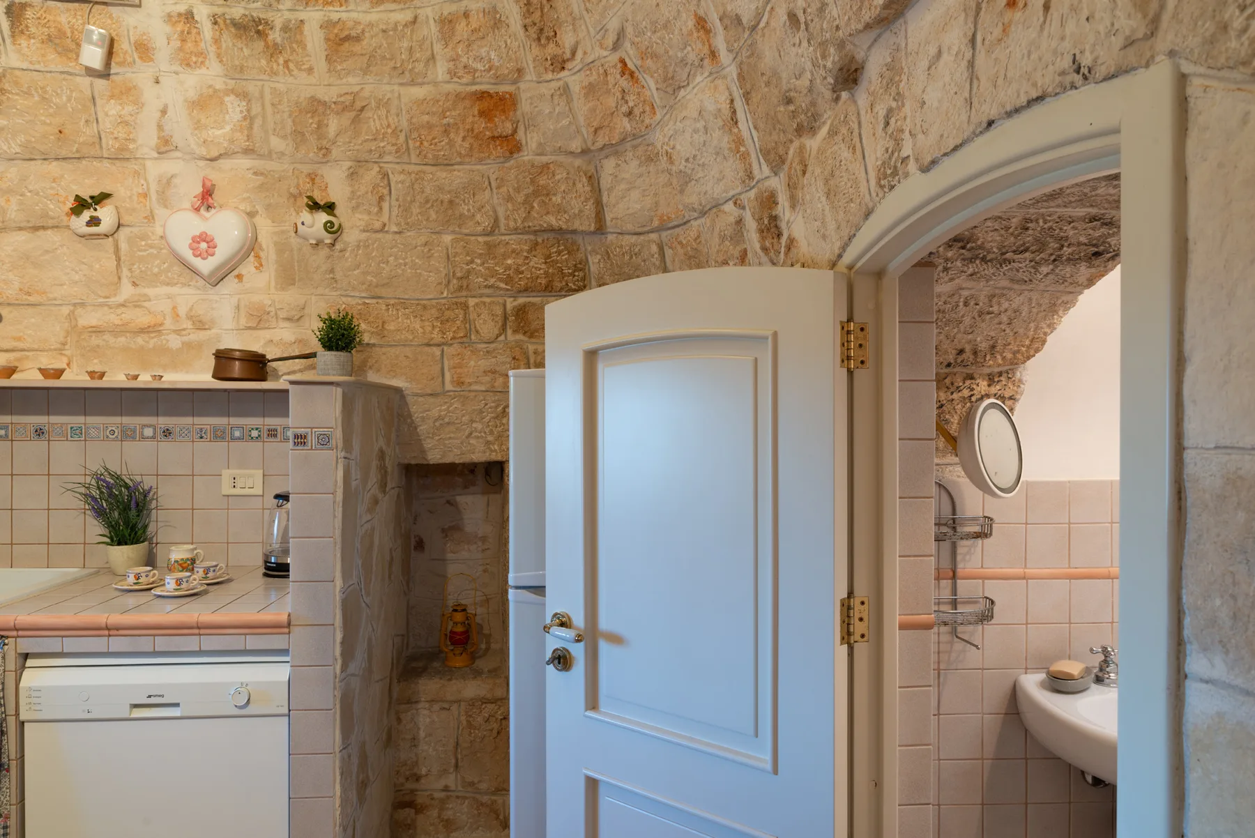 Interior de paredes de piedra con una puerta abierta que da a un baño con azulejos.