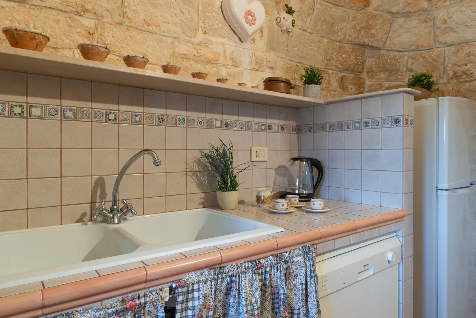 Una encimera de cocina alicatada con fregadero, hervidor y refrigerador.