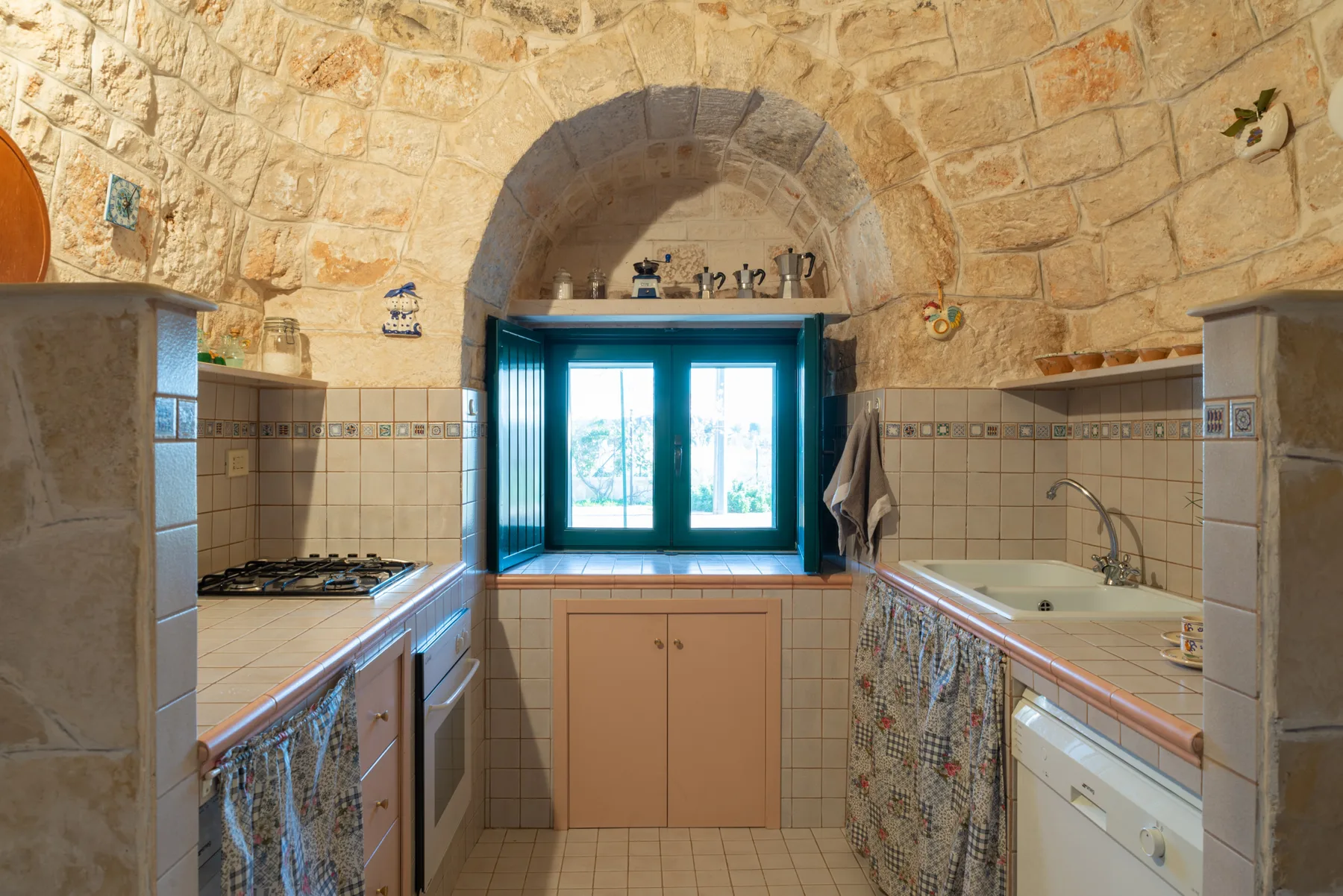 Una cocina rústica con una ventana central, encimeras de azulejos y un fregadero.