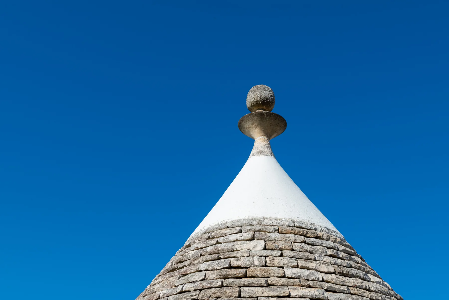 Un tejado cónico de piedra coronado por una estructura blanca puntiaguda contra el cielo azul.
