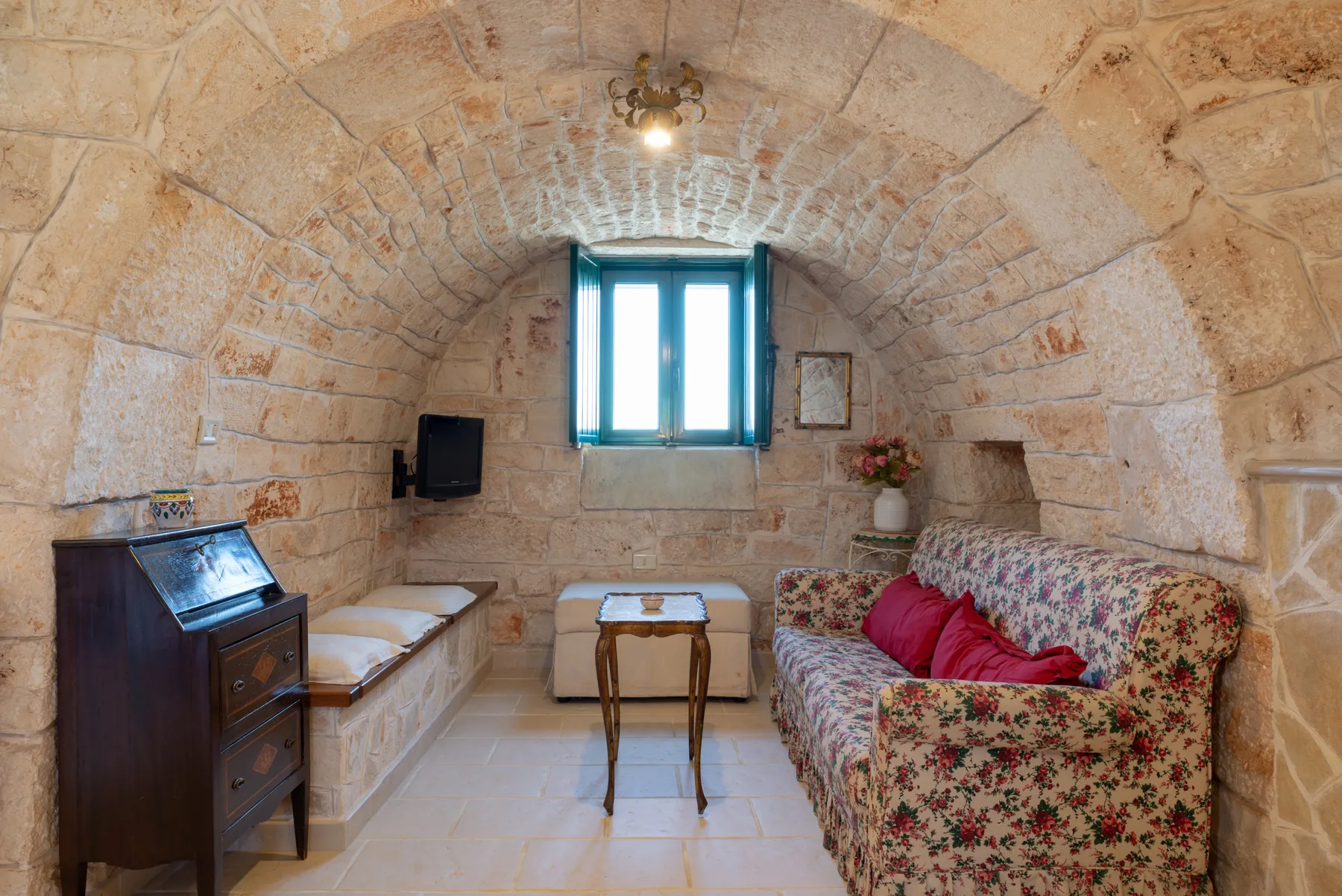 Una habitación de piedra con una ventana pequeña, asientos y una mesa de madera.