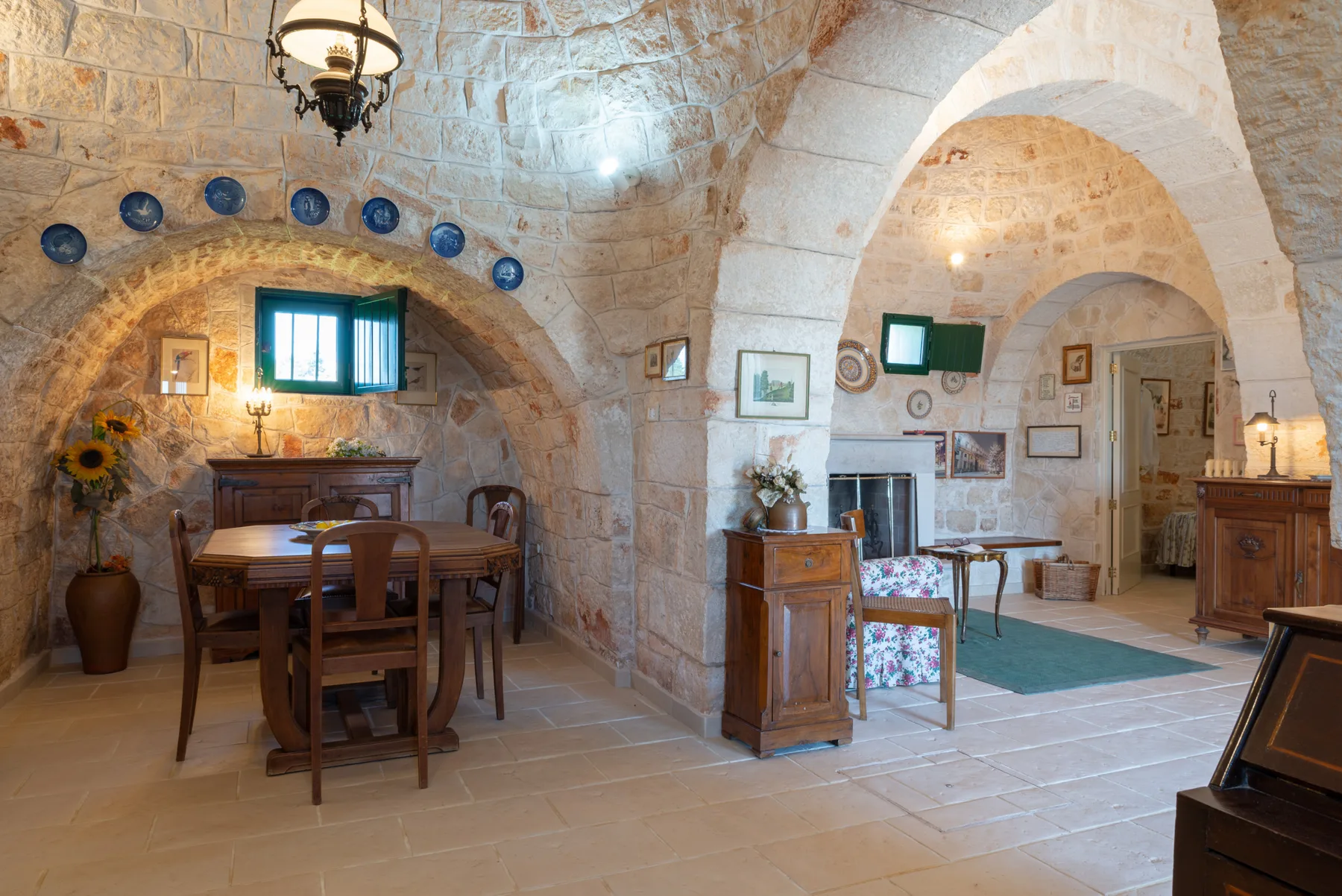 Interior de piedra con techos abovedados, una mesa de comedor y cuadros.