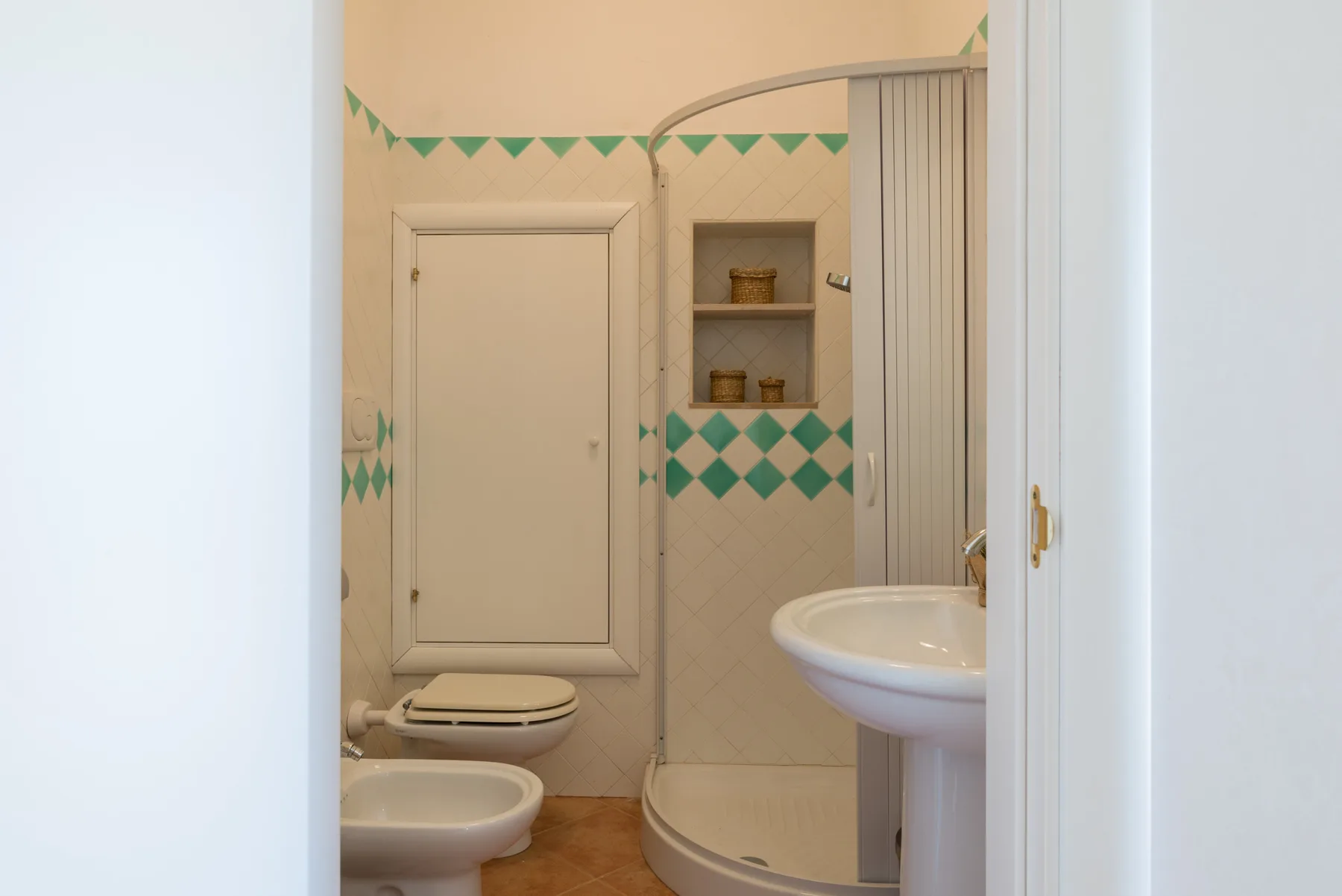 Un baño con ducha, lavabo y azulejos verdes con patrón de rombos.