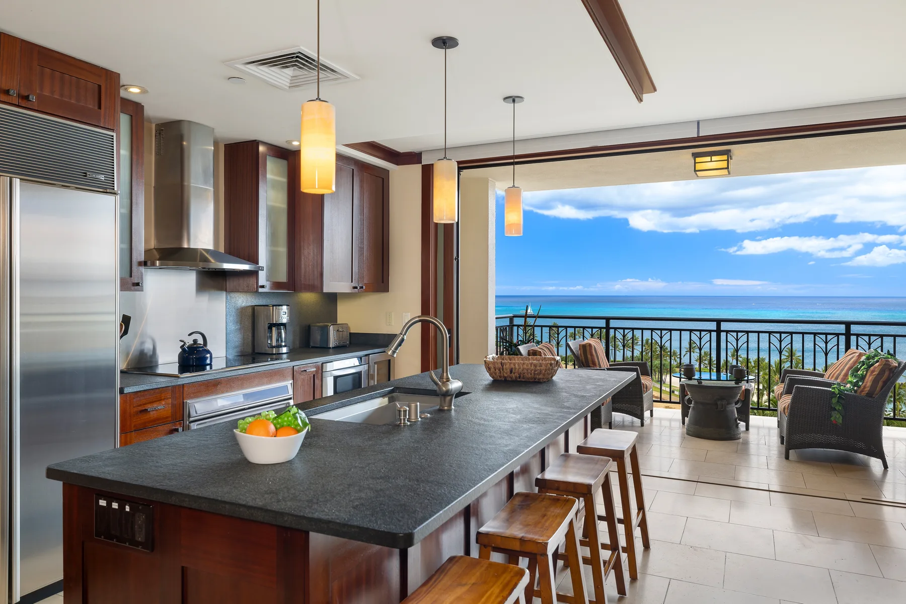 Una isla de cocina con asientos da a un balcón con vistas al agua.