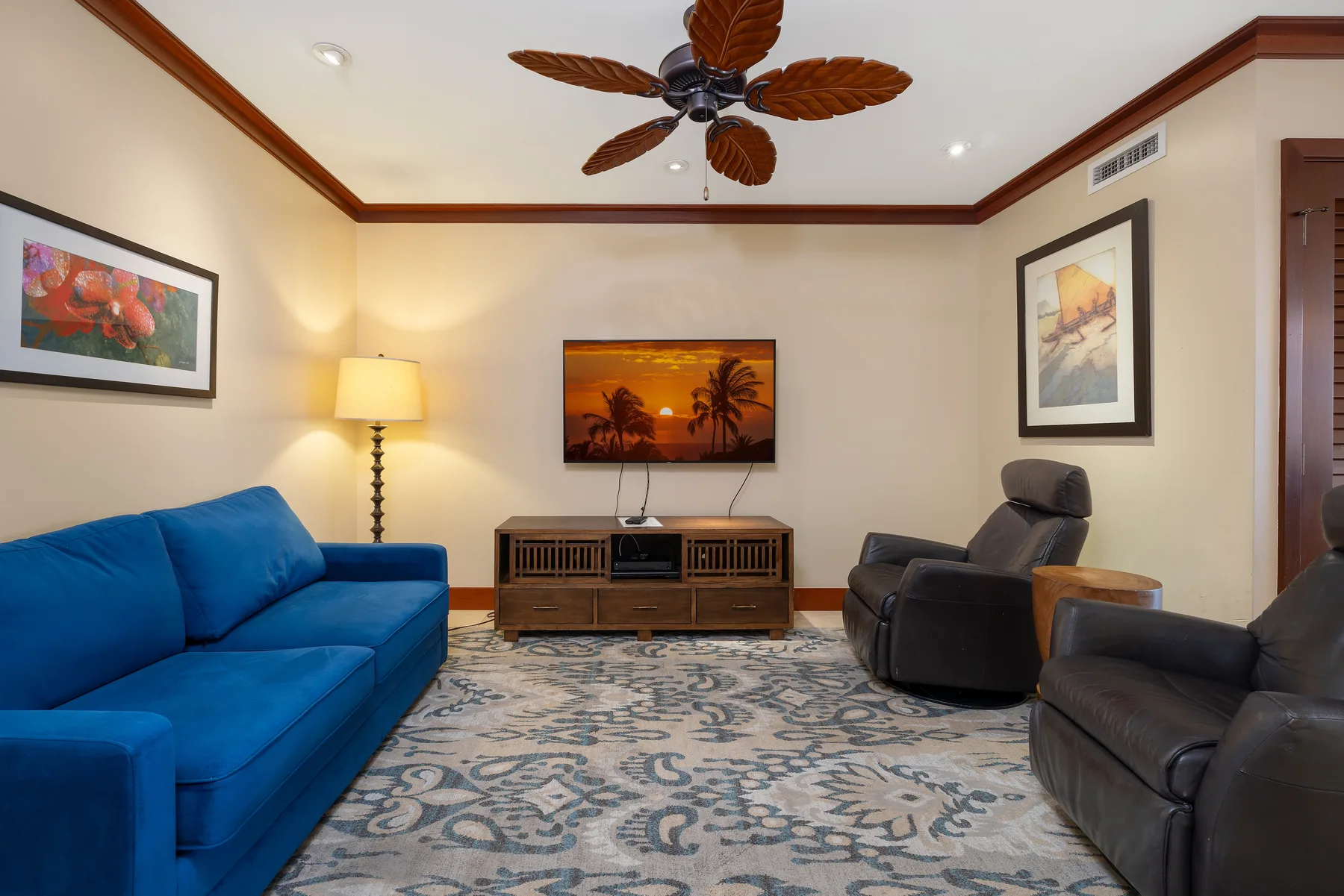 Una sala de estar con asientos azules, sillones oscuros y un televisor en la pared.