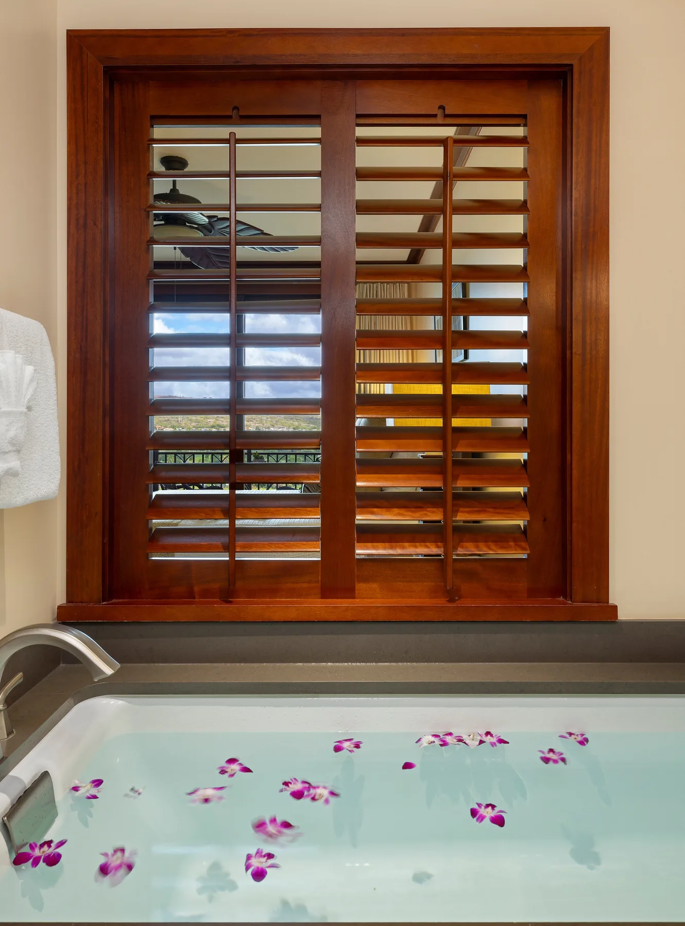 Una bañera de baño está bajo una ventana con contraventanas de madera, con pétalos flotando en el agua.