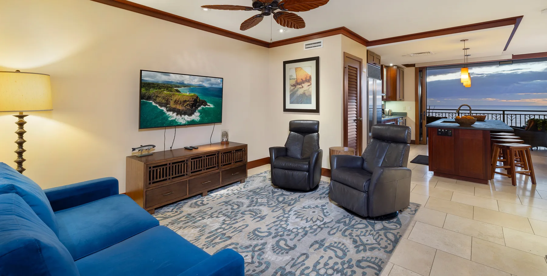 Una sala de estar con asientos azules y sillones reclinables se abre a una cocina y comedor.