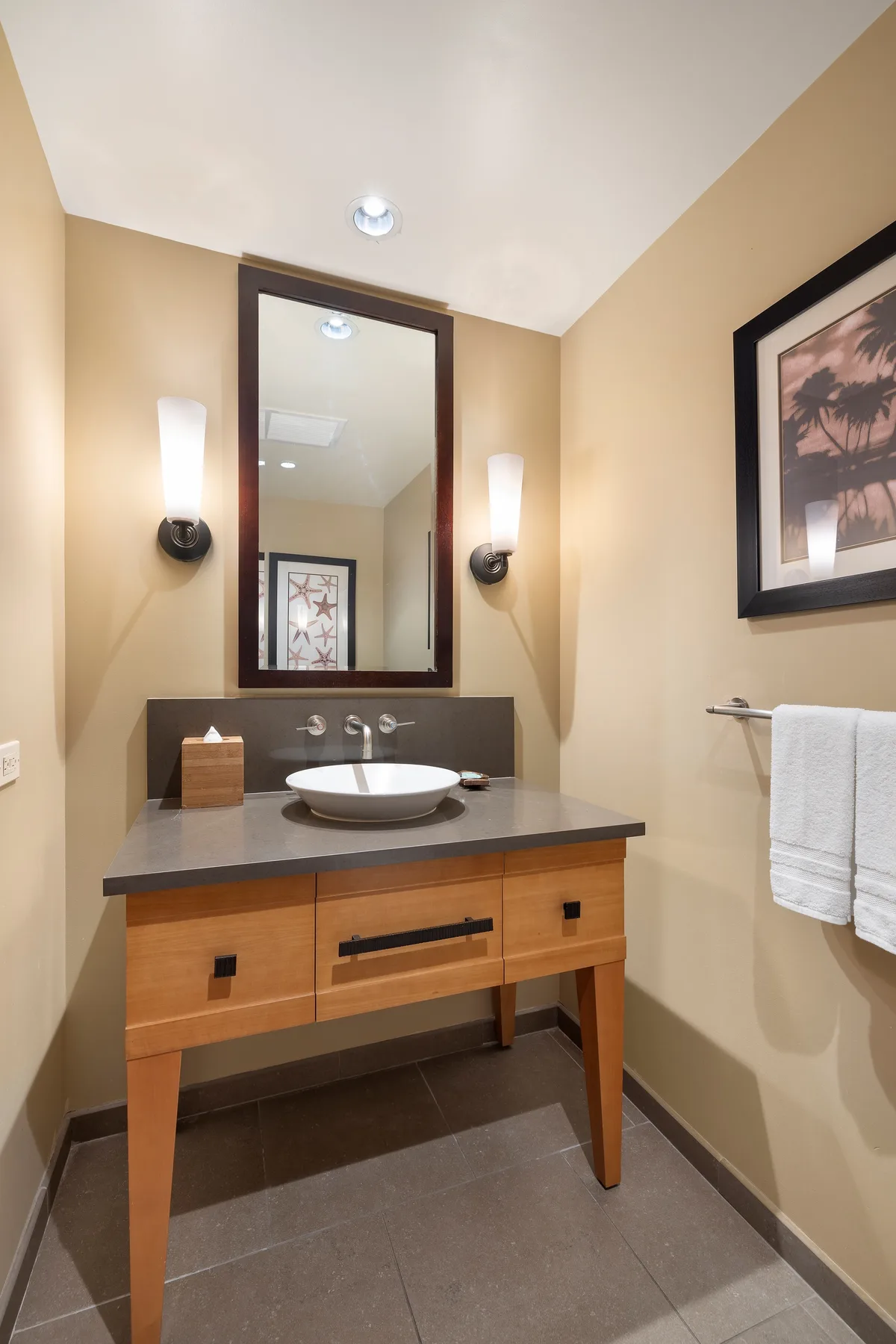 Un lavabo de baño con espejo, luces de pared y un cuadro enmarcado.