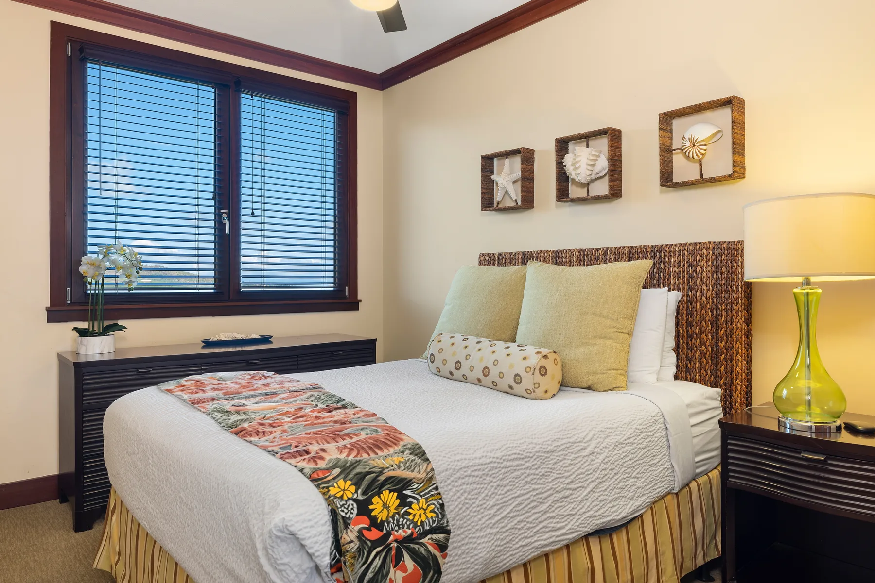 Un dormitorio con una cama bien tendida, una manta estampada y una ventana con persianas.