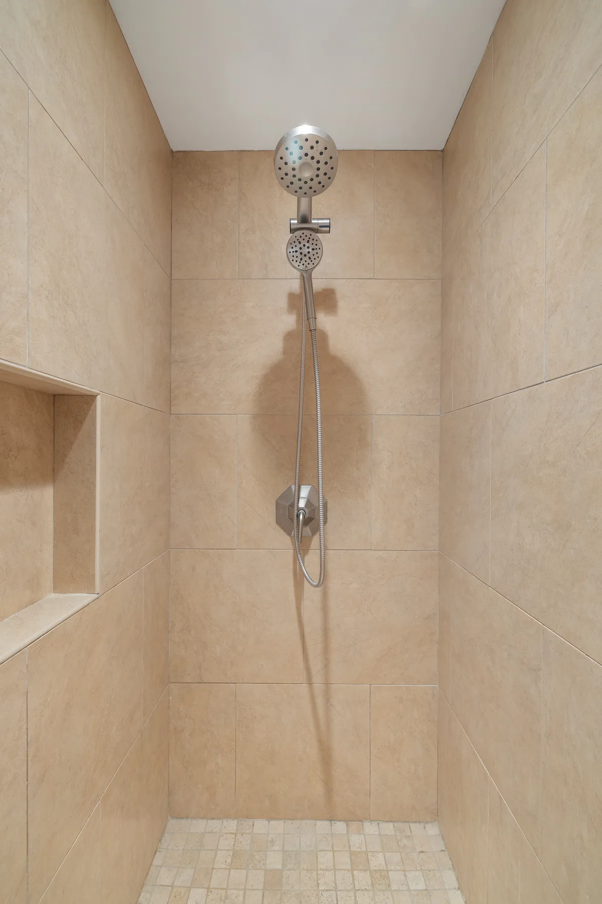 Una ducha con azulejos, una ducha de mano y un nicho empotrado en la pared.