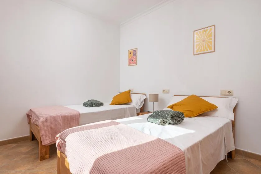 Un dormitorio luminoso con dos camas vestidas con ropa de cama blanca y rosa.