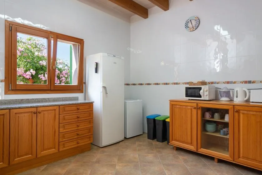 Una cocina con gabinetes de madera, un refrigerador y una ventana con vista a vegetación.
