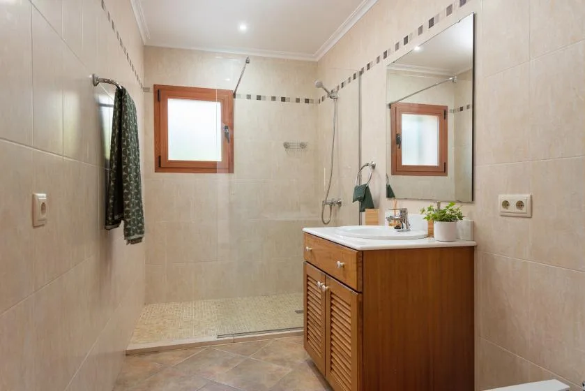 Baño con azulejos, mueble de madera, espejo y zona de ducha.