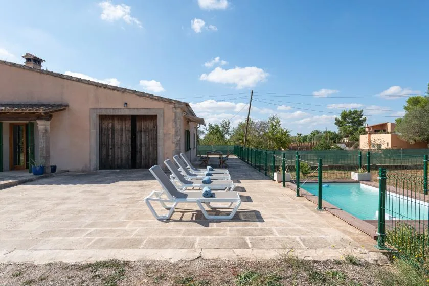 Un patio soleado con asientos junto a una piscina cercada.