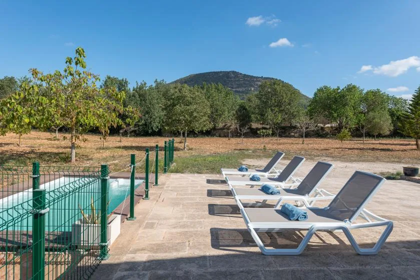 Un patio junto a la piscina con tumbonas da a un paisaje verde y arbolado.