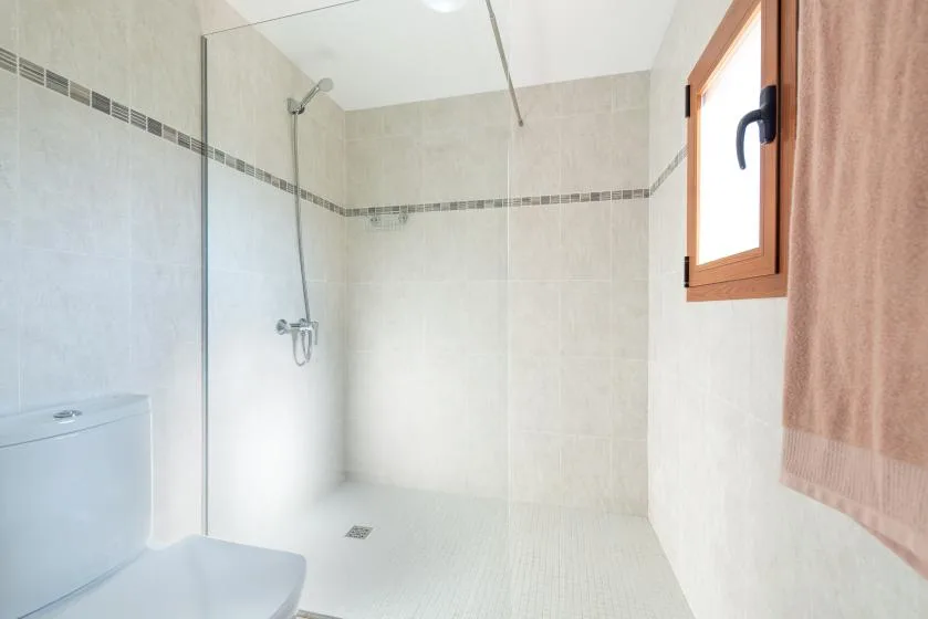 Un baño alicatado con ducha a ras de suelo y una ventana pequeña.