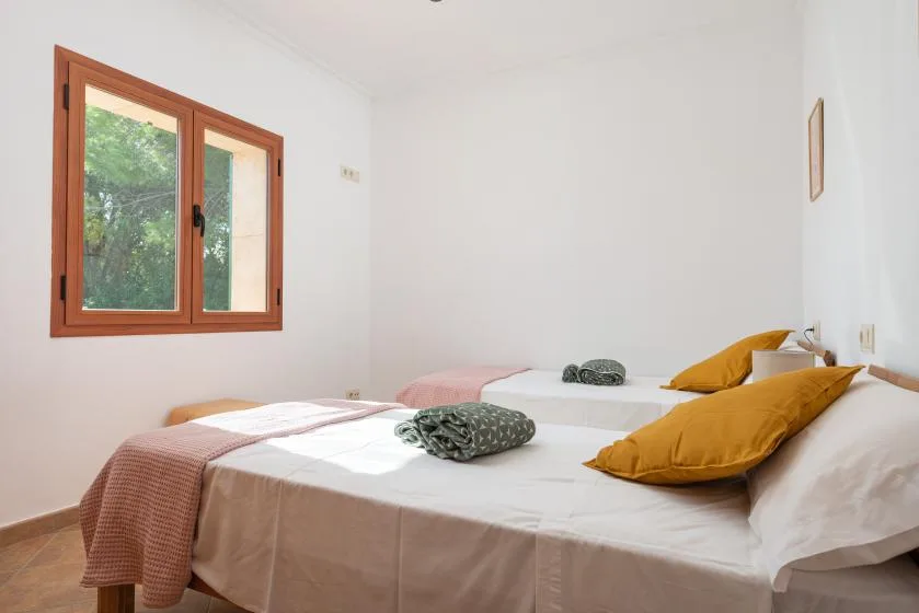 Un dormitorio luminoso con dos camas y una ventana con vistas a la vegetación.
