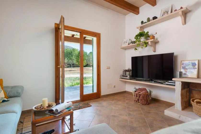 Una sala luminosa con televisor, puertas de vidrio abiertas y asientos.